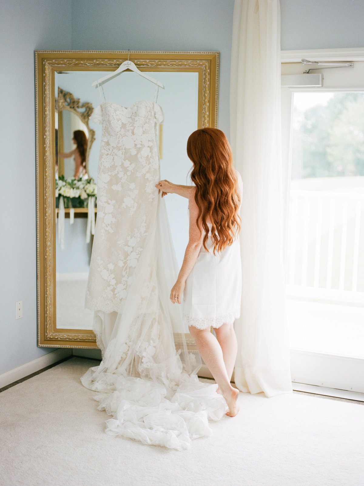 bride looking at wedding dress hanging on mirror at lancaster pa wedding