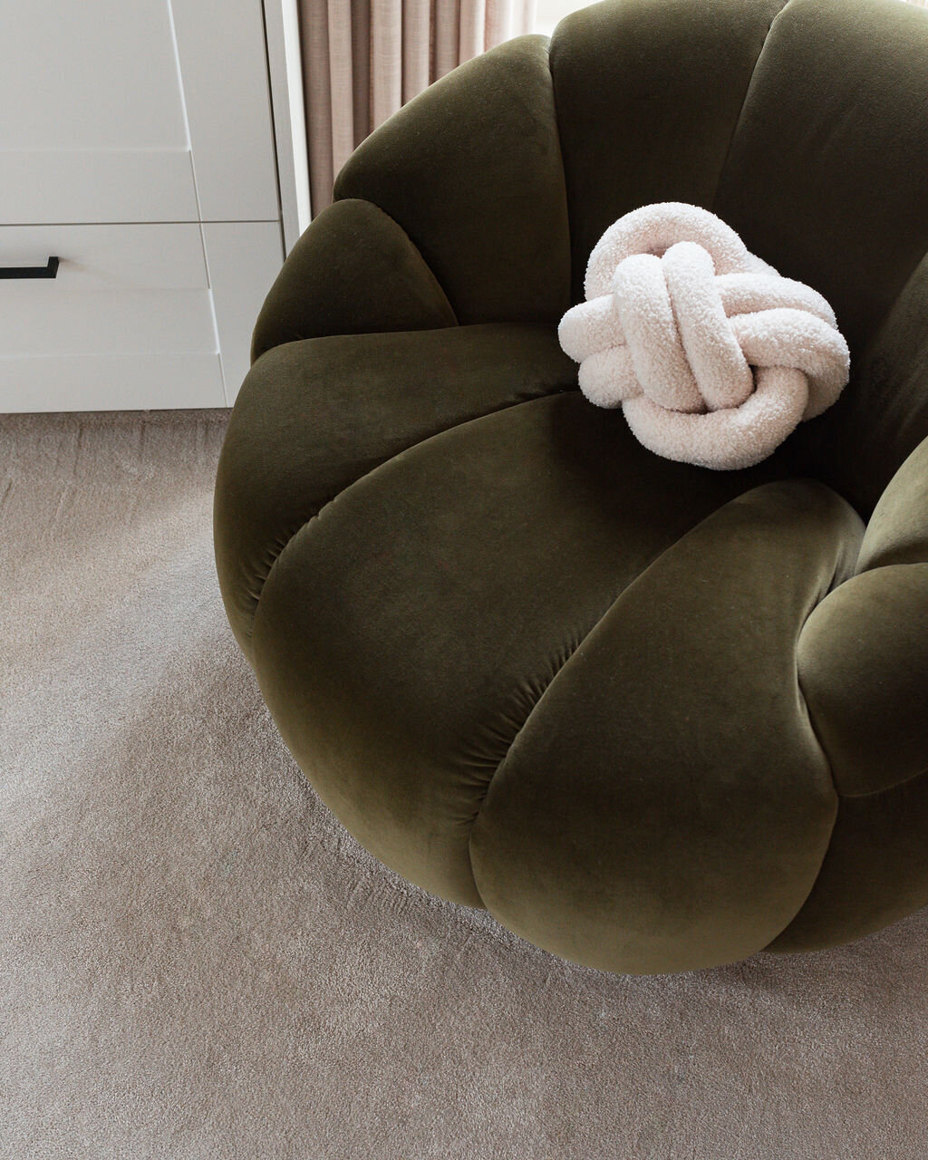 A cozy, round green velvet chair with a plush white knot pillow.