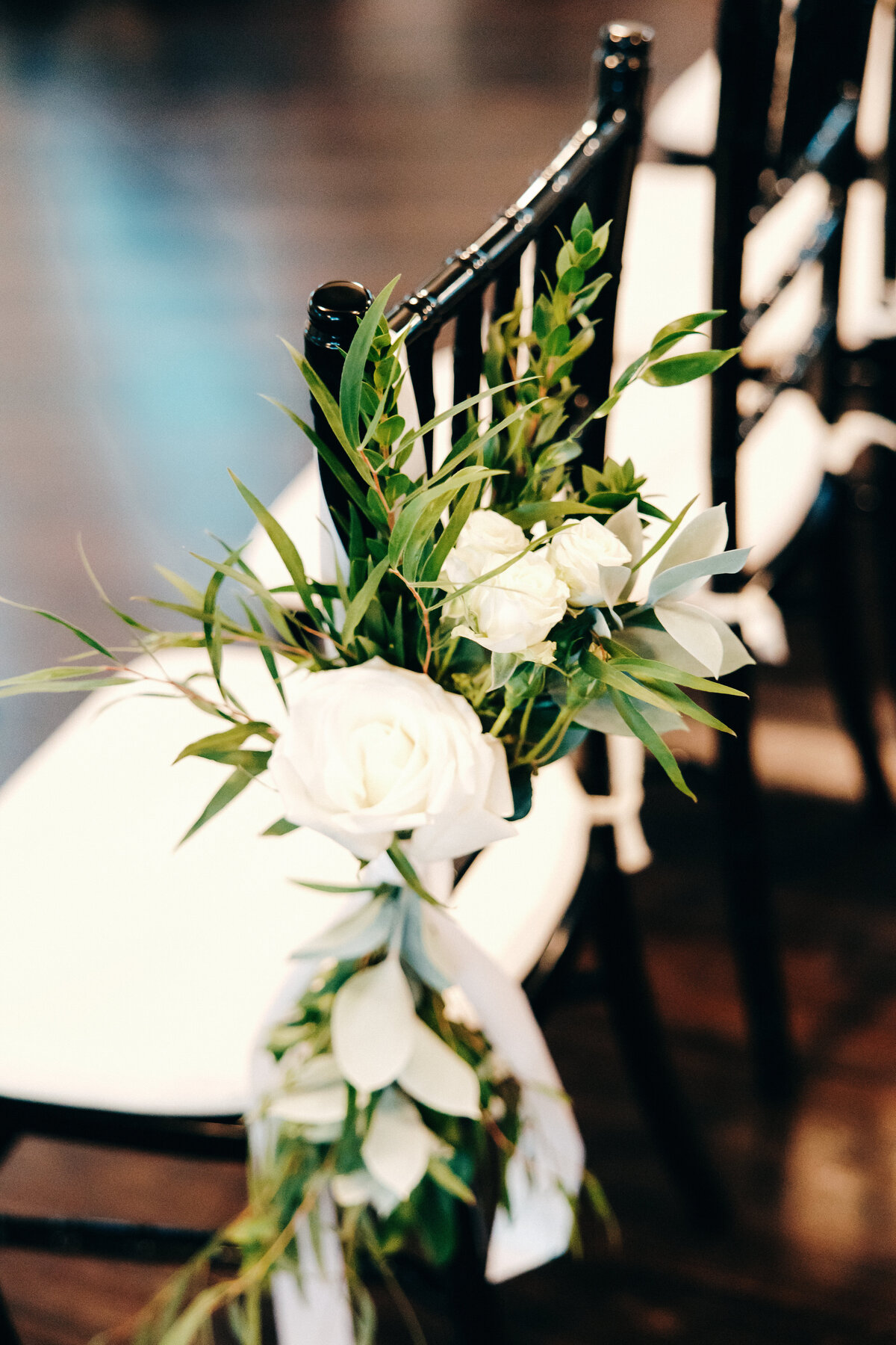 White wedding ceremony floral and greenery chair ties.