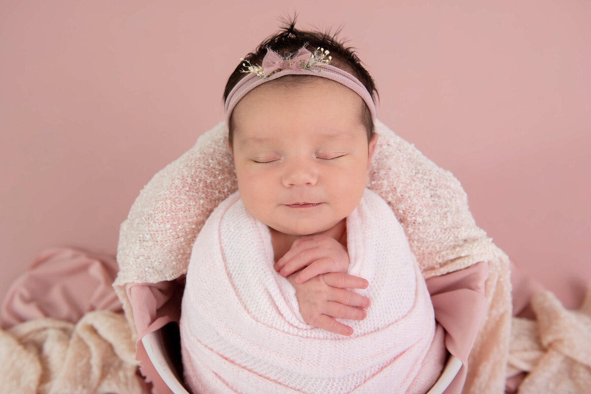 newborn baby girl wrapped in pink in a pink bucket on a pink background for her newborn photography session in Burlington, ON