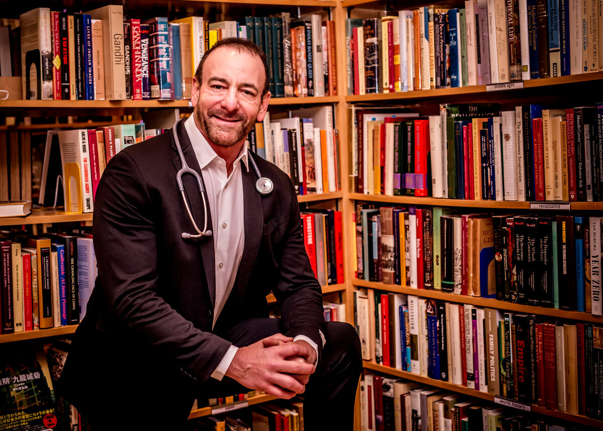 A male doctor wearing a suit & stethoscope looking off in a library setting while posing for a South Shore MA branding photographer