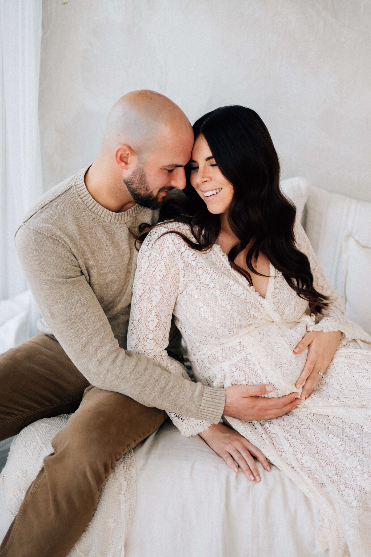 mother and father sitting on a bed holding the mothers pregnant belly