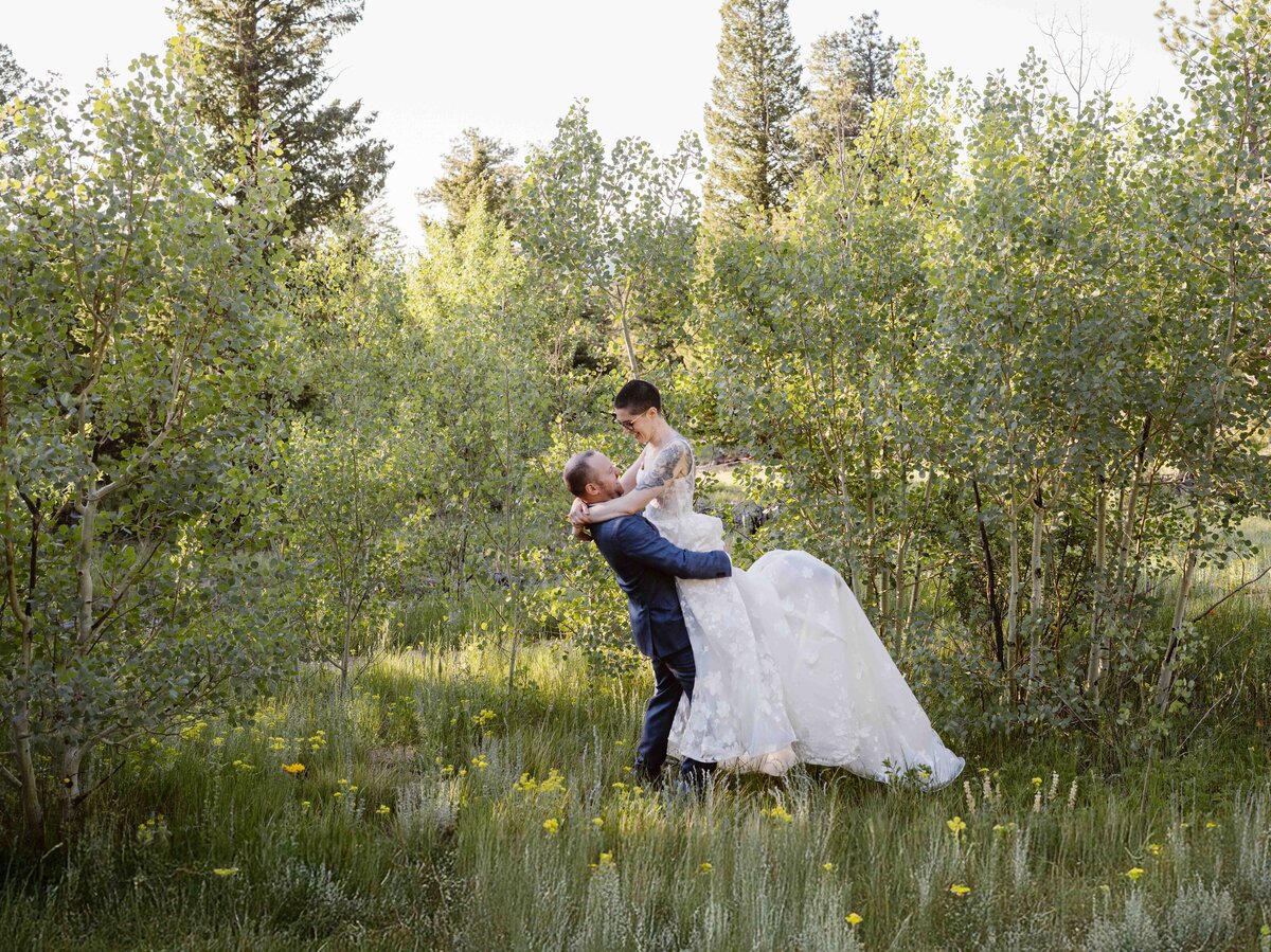 Groom picks up bride in a meadow during their sunrise elopement in Estes Park, Colorado.