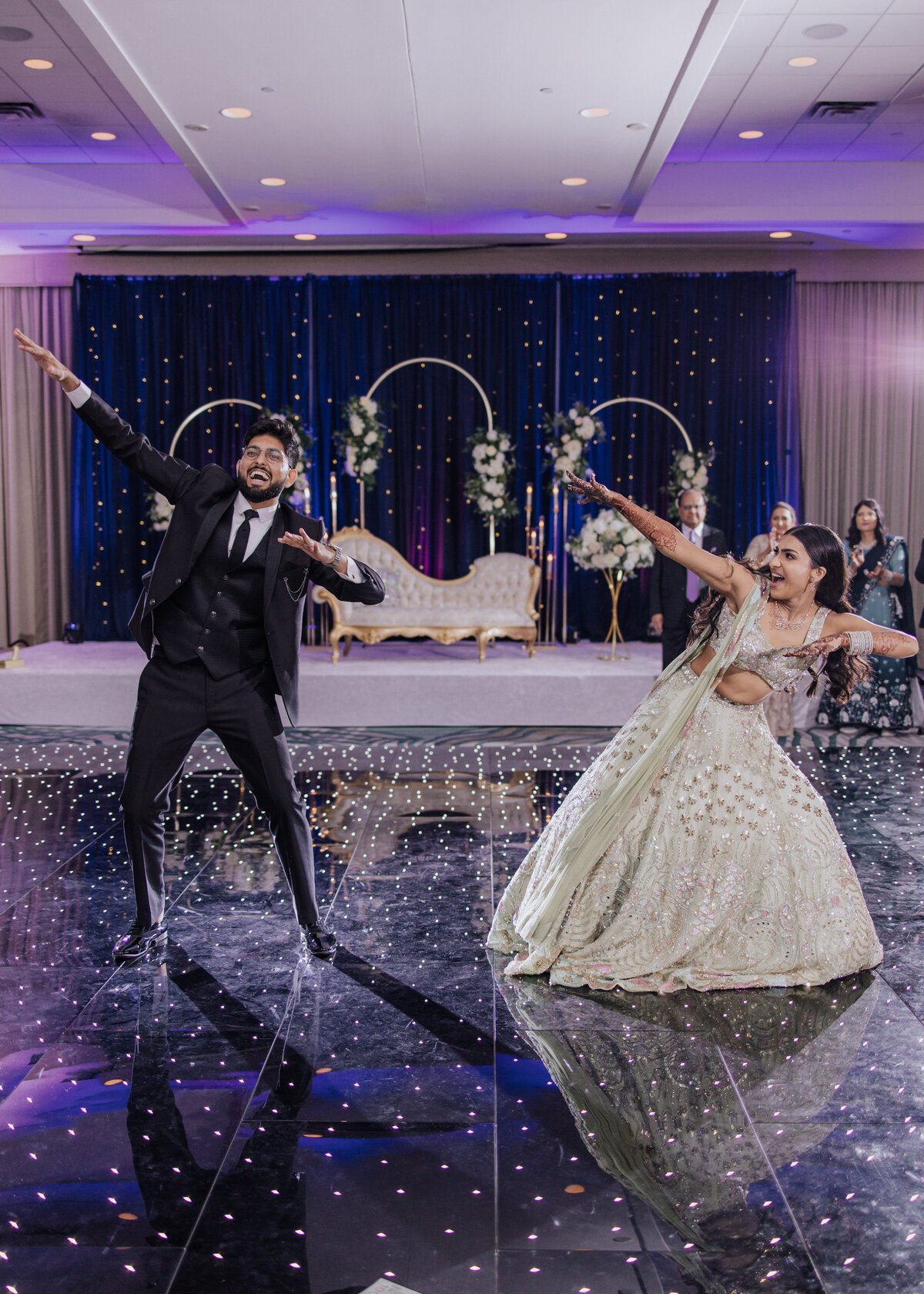 Couple performing a fun dance on a sparkling Sangeet dance floor during their South Asian wedding celebration.