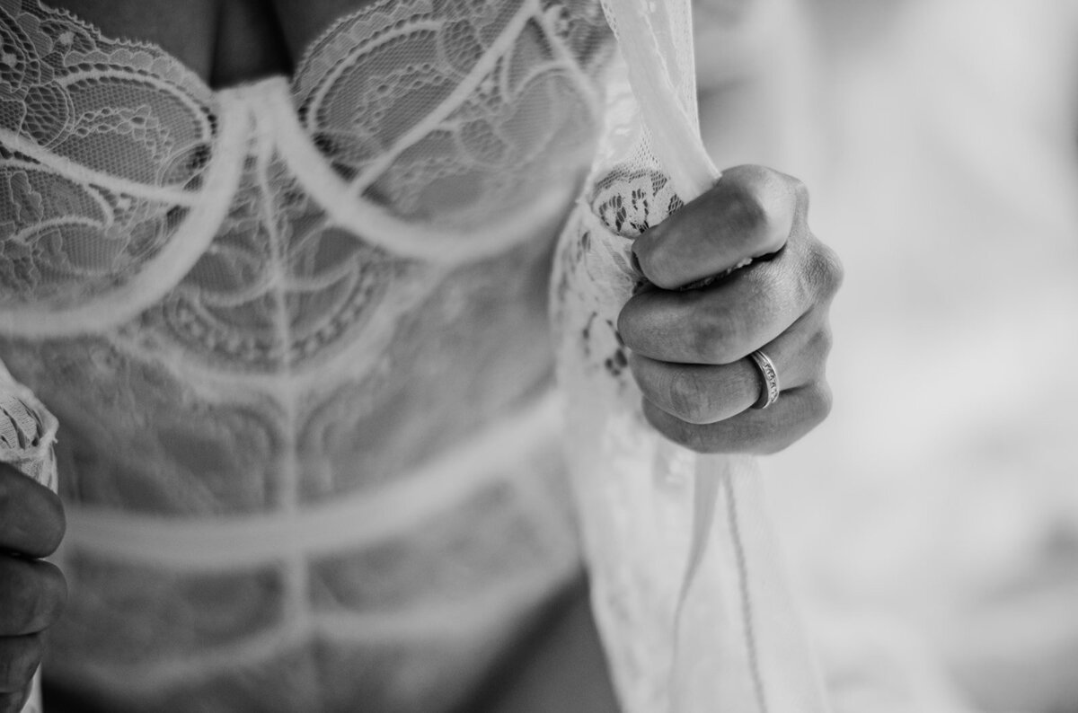 bridal boudoir session with woman wearing a one piece with white lace and holding a silk robe over her shoulders captured by Baltimore photographers
