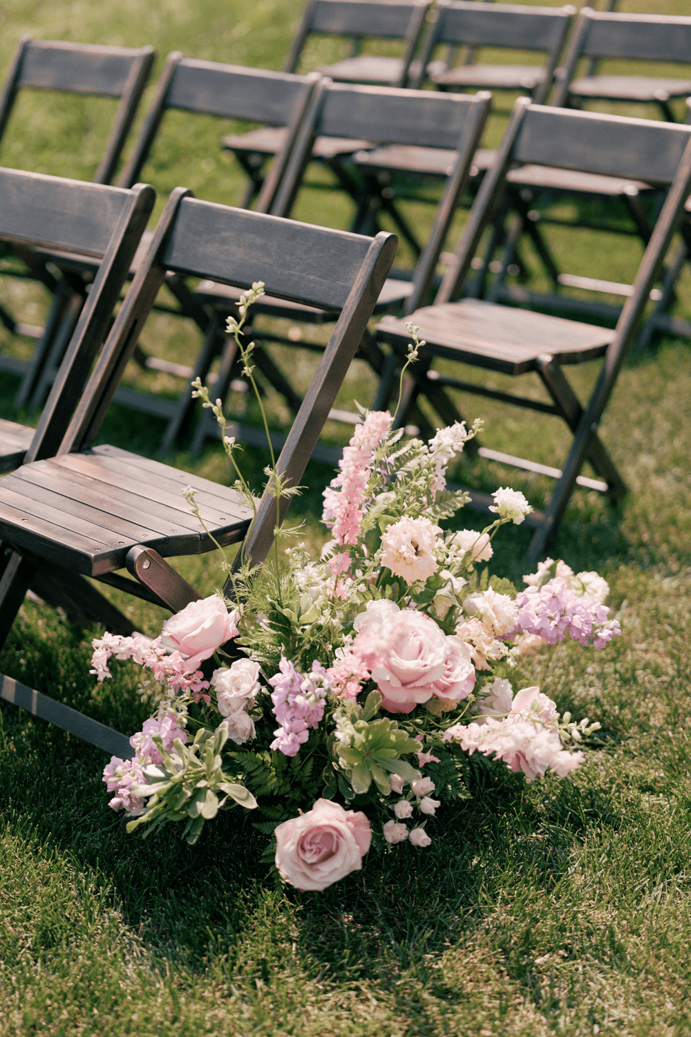 Pastel floral aisle arrangement next to wooden ceremony chairs at a summer wedding at Moonlight Basin, featuring roses, snapdragons, and lisianthus.