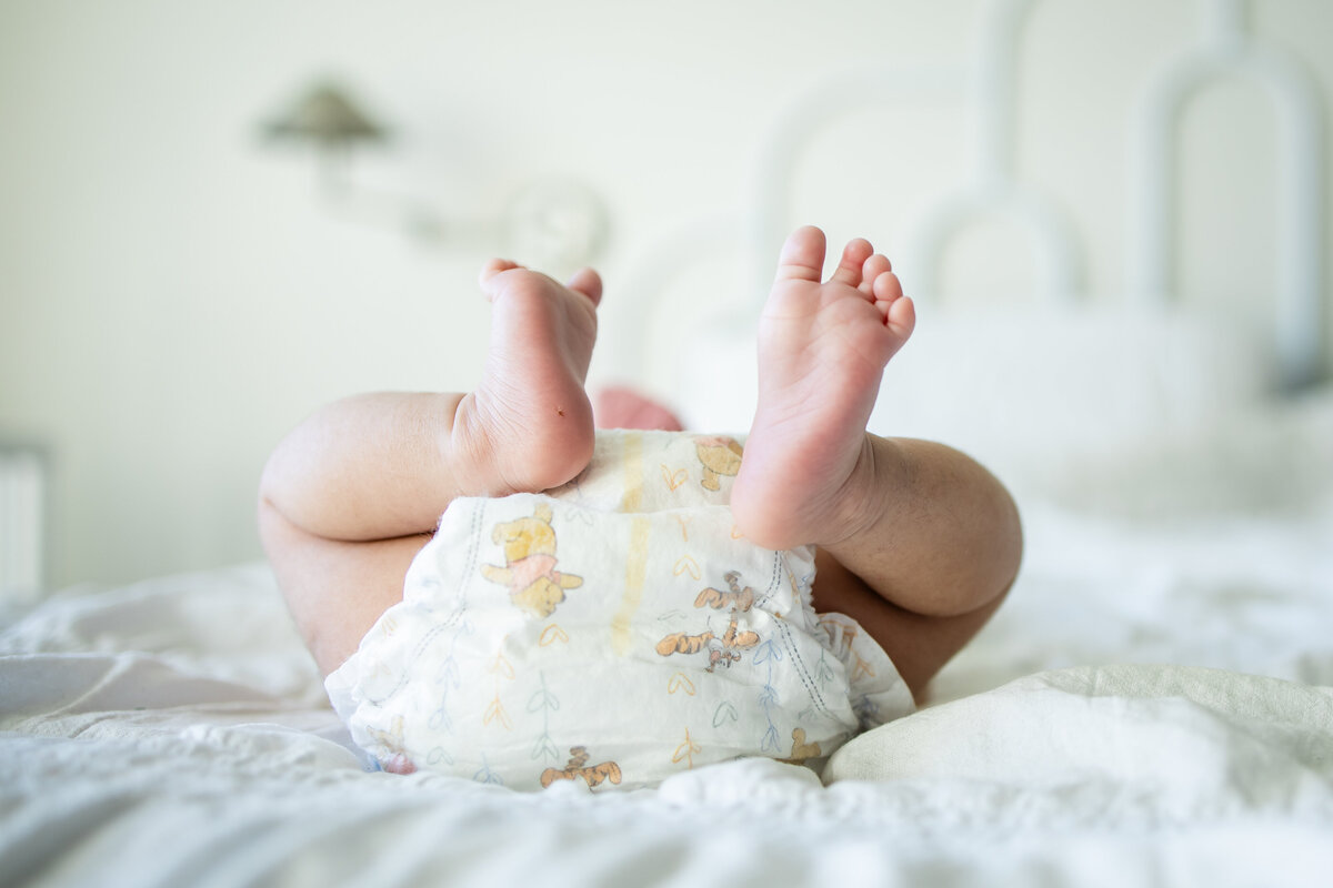 Baby laying on white bed in diaper with feet in the air