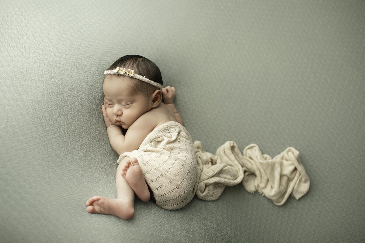Newborn baby girl wrapped in a soft white swaddle, captured from a side angle as she peacefully sleeps, highlighting her delicate features in a timeless and serene portrait