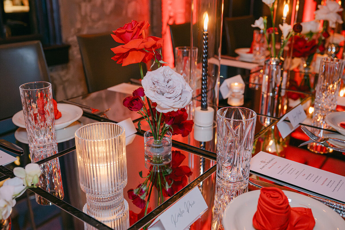 Tabletop editorial showing glass candle holders and roses in red-toned reception room at The Battalion