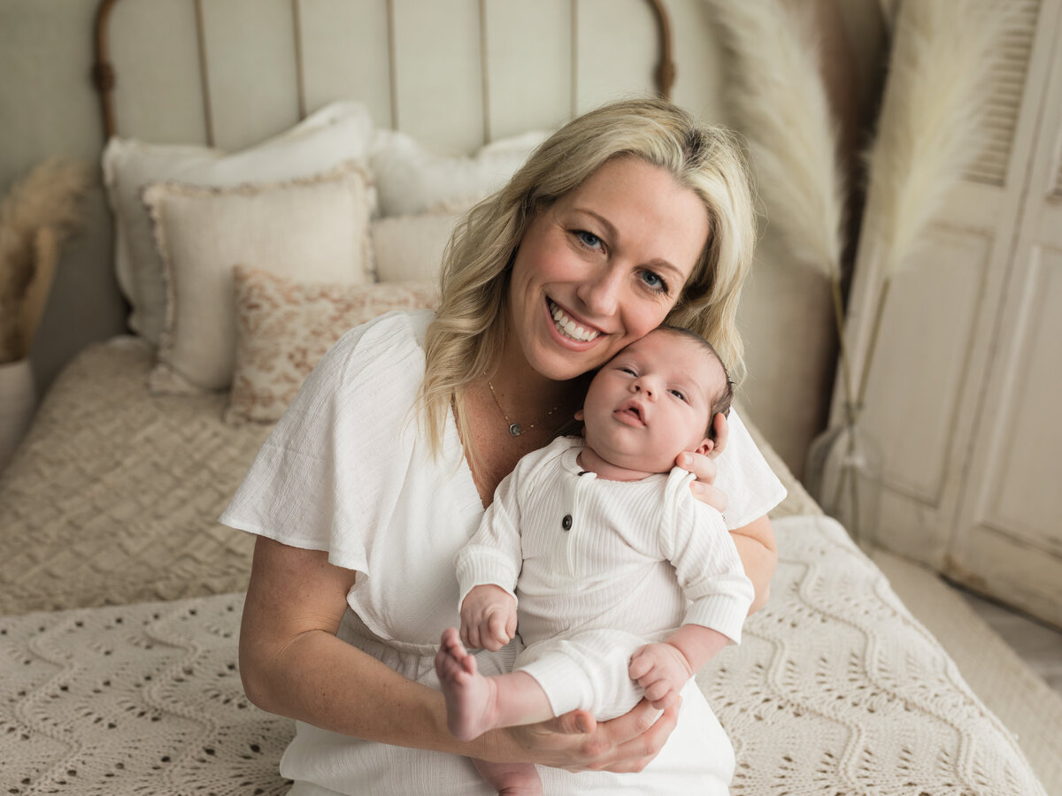 mom holding newborn baby boy in white onesie for studio lifestyle session cleveland newborn photographer