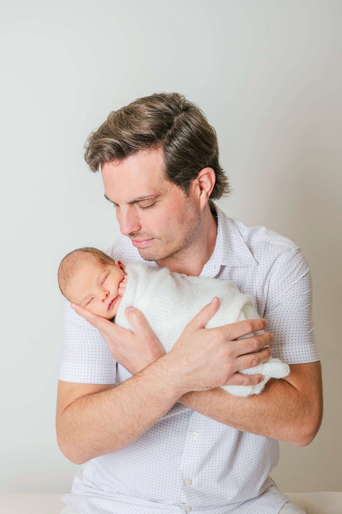 Dark haired dad holding his newborn baby in his arms.