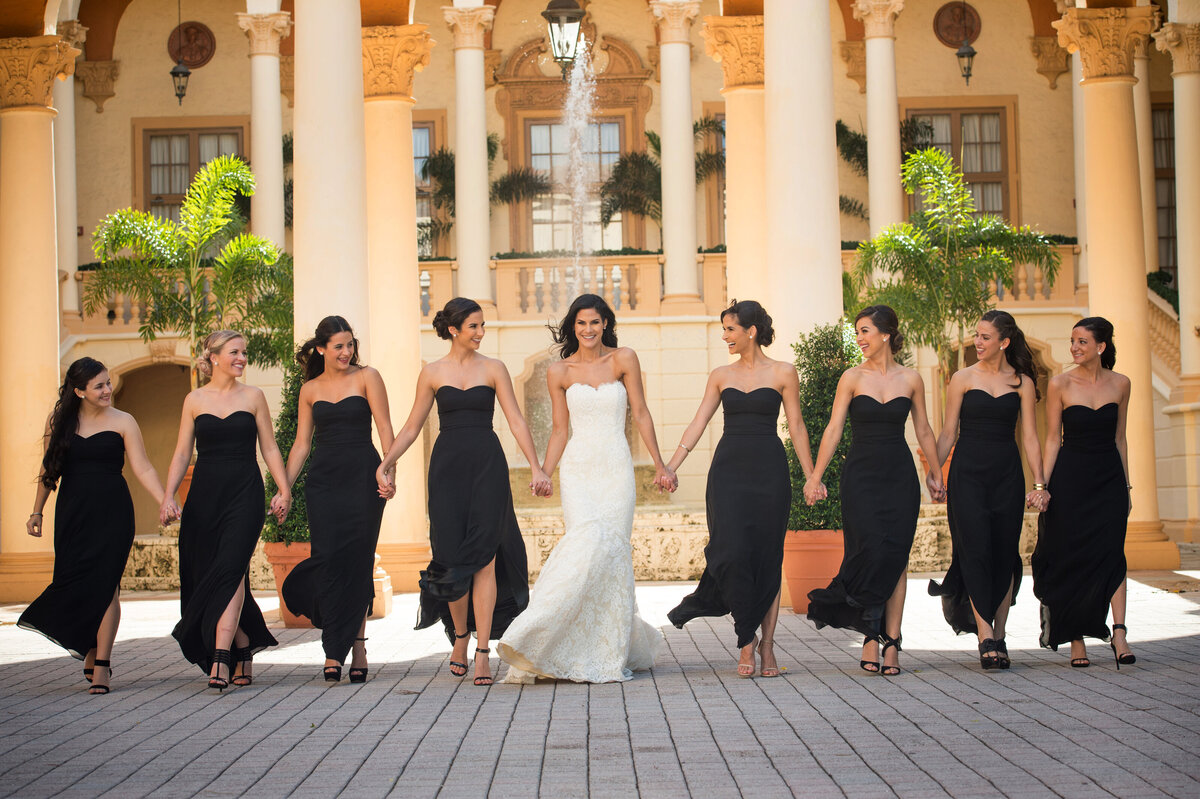 Bride and bridesmaids holding hands in front of a grand venue, photographed by Rodrigo Varela Photography.