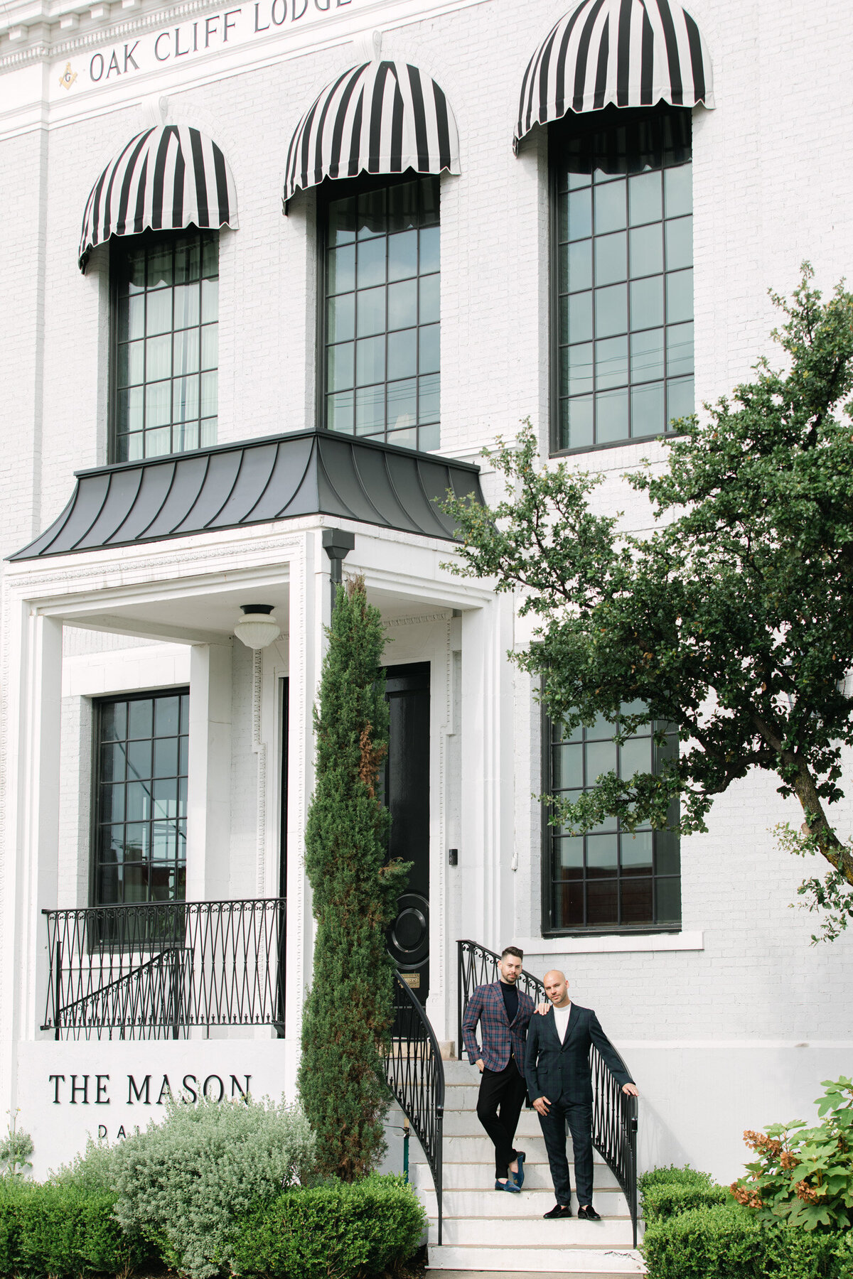 Two grooms on the steps of The Mason in Dallas during their engagement session, posed in a refined and elegant style