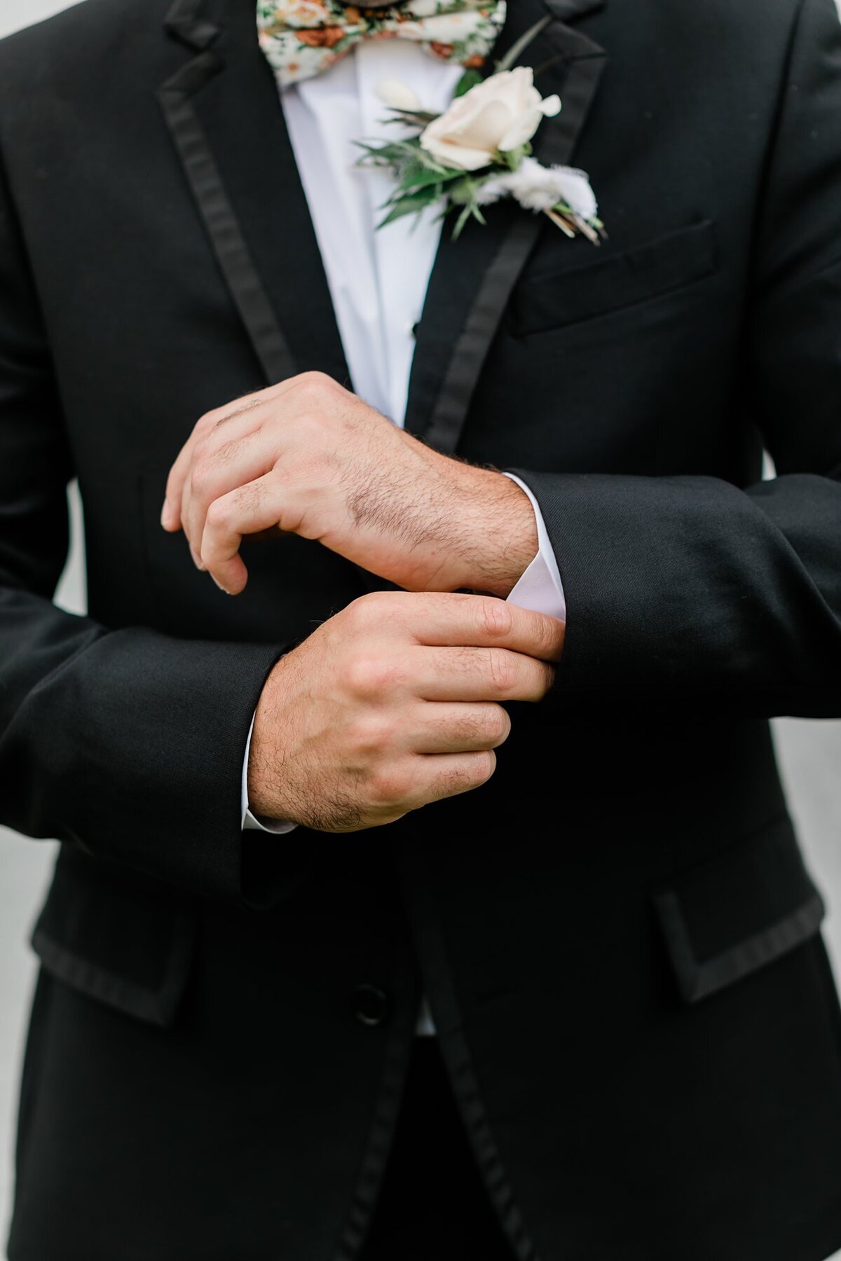 Close up of groom in a black tux adjusting his cuffs for his wedding portraits at Olde Dobbin Station.