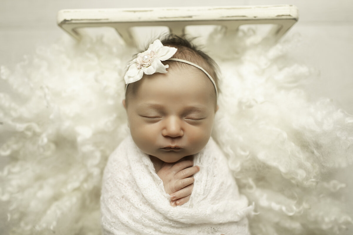 Newborn baby girl peacefully resting on a soft bed adorned with delicate ruffles, creating a dreamy and elegant portrait