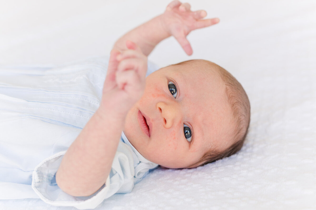 newborn looking at his hands laying on bed