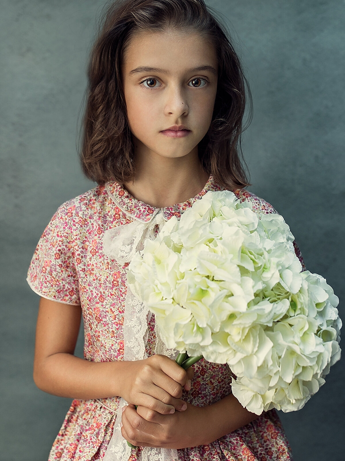 A portrait of a girl holding  a bunch of white flowers looking at the camera