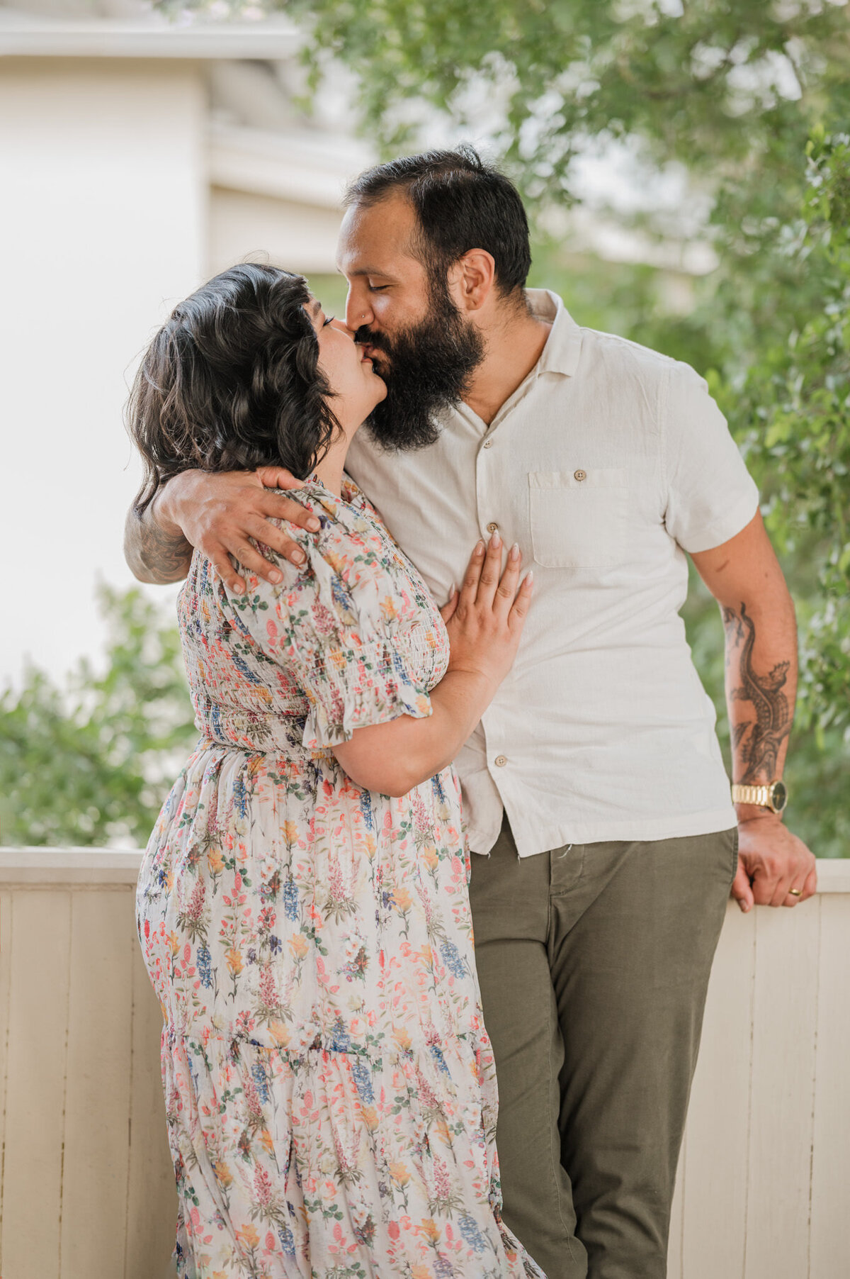 A man and woman lean against a porch rail and kiss.