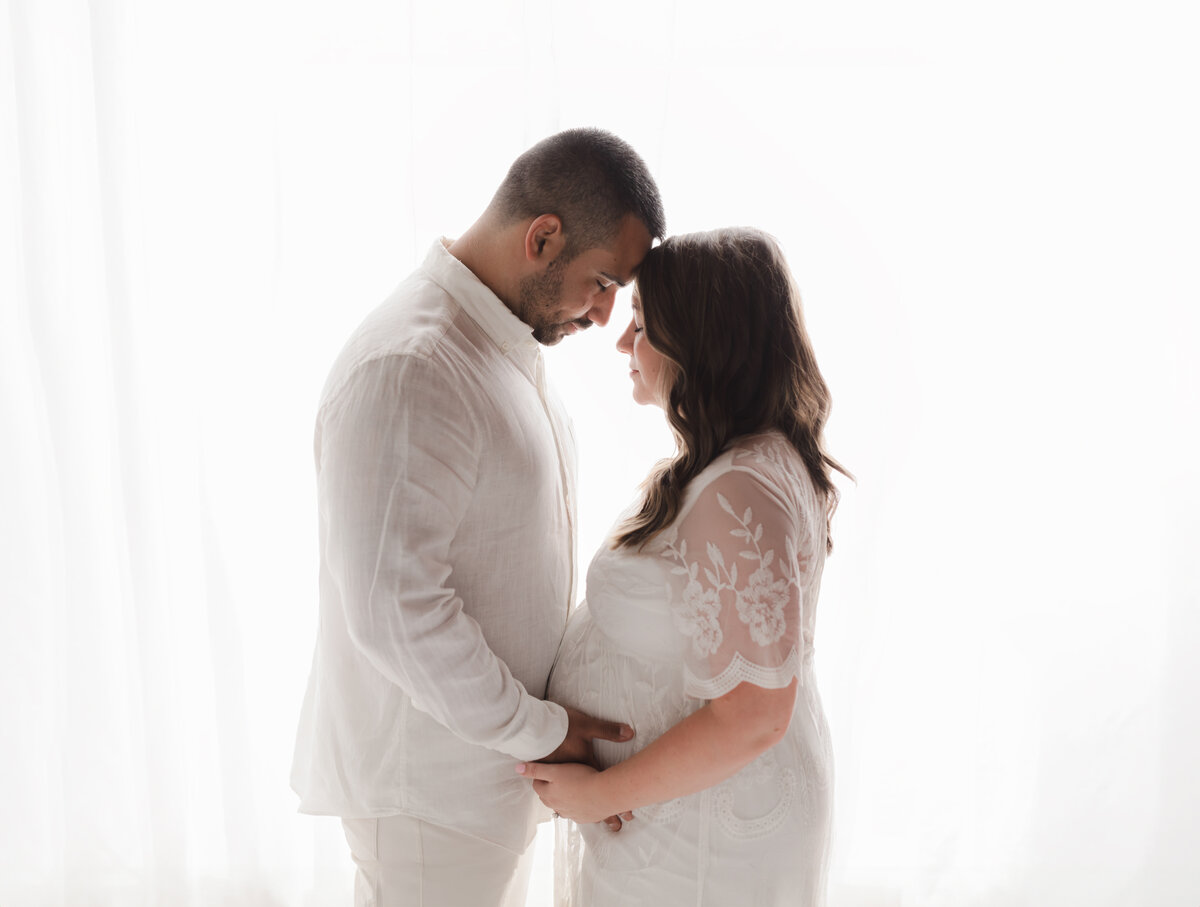 husband and wife holding pregnant belly for maternity studio photoshoot