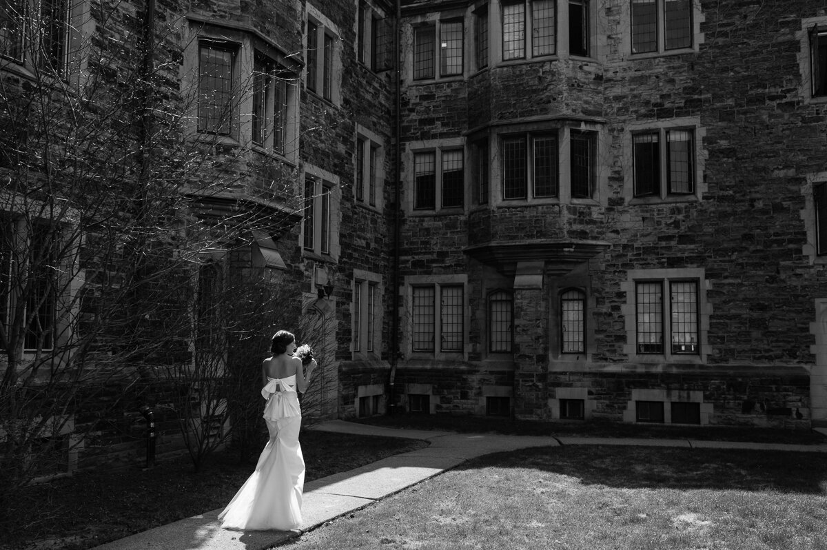 Classic black and white photo of a bride walking in the sunlight with a large bow on the back of her gown