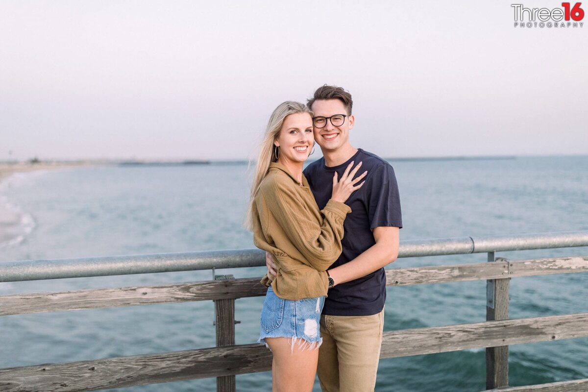 Smiling engaged couple pose together on the Seal Beach Pier