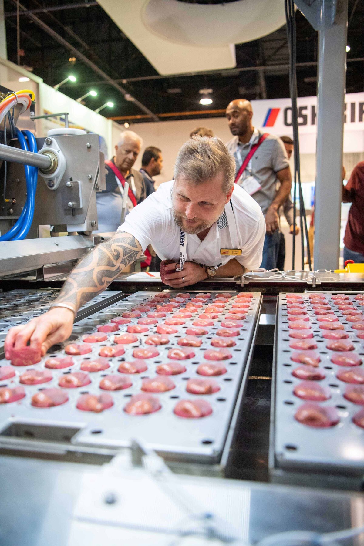 A man reaches to remove  cupcakes from a machine as people look on from behind