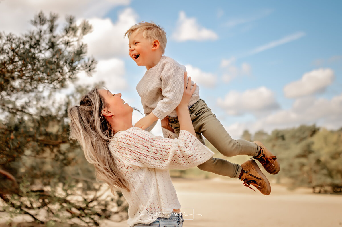 Mama gooit zoon lief de lucht in en de jongen lacht bij de duinen van Herperduin
