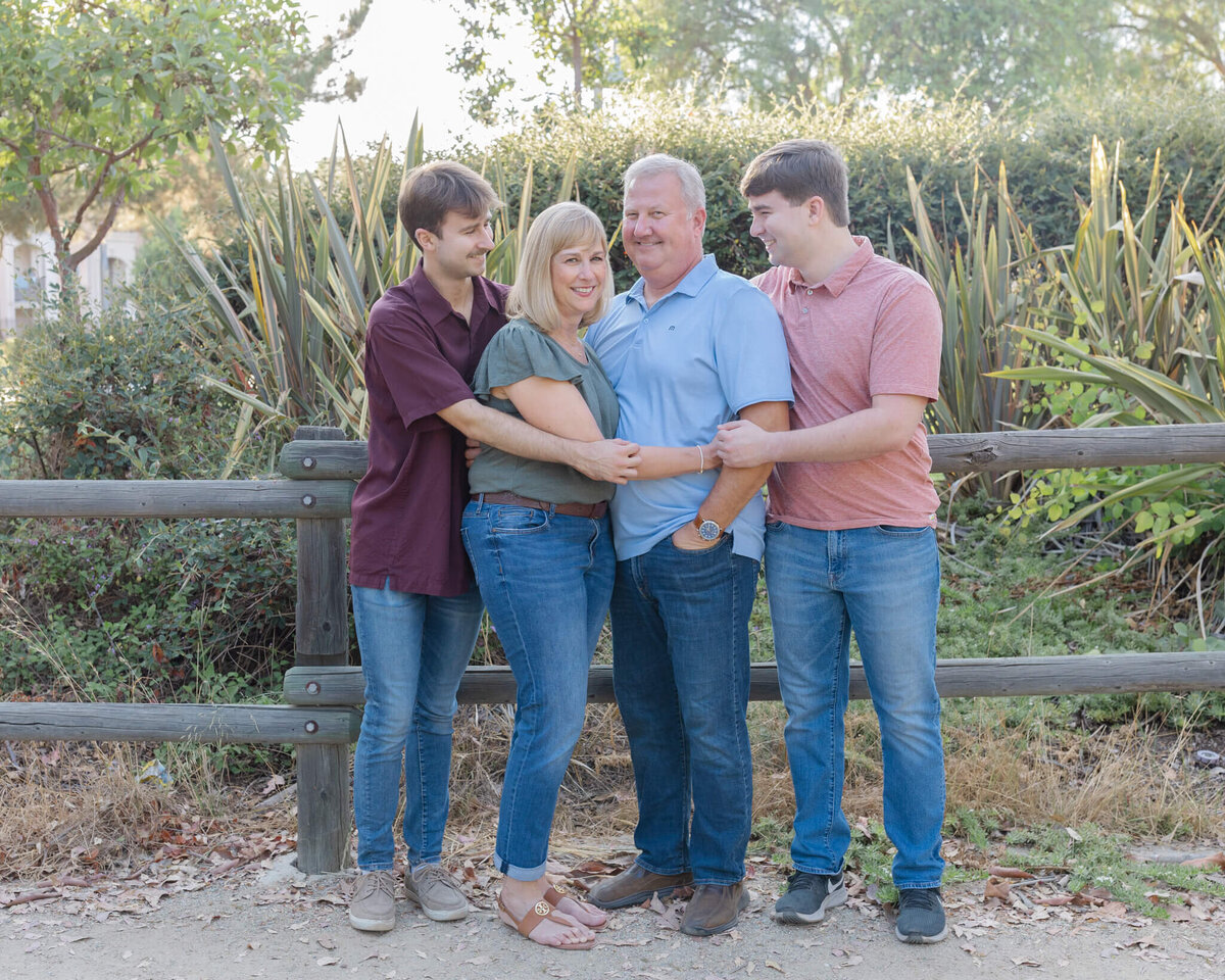 A family of four looking at each other with their arms around each other laughing at Citrus Ranch Park.