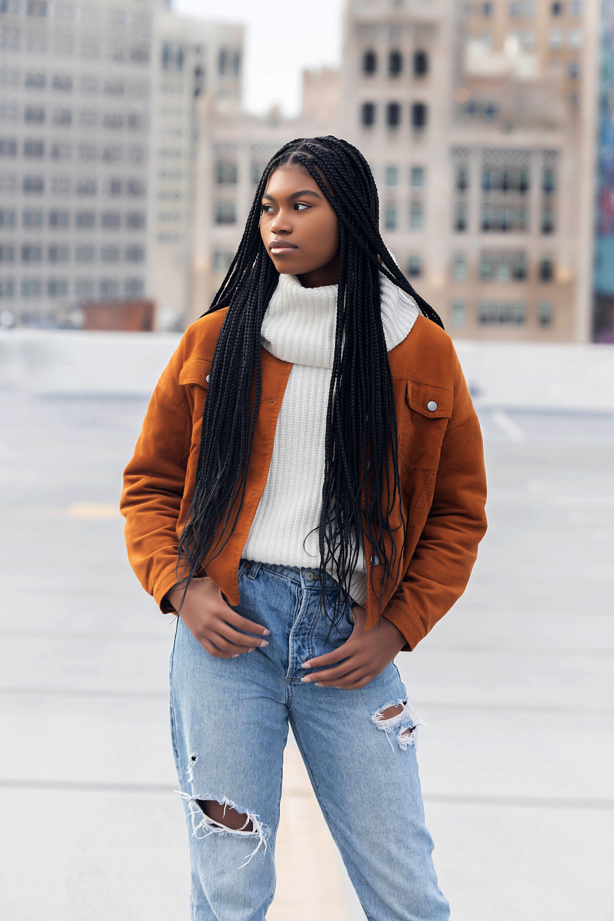 The Belt in Detroit Senior Photoshoot | Detroit Michigan Senior Photographer, Senior girl with braids wearing sea green long sleeve crop top and black destructed jeans posing casuallt sitting at a table