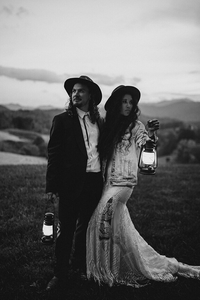 bride and groom pose facing away from each other in the outdoors while each holding a lamp