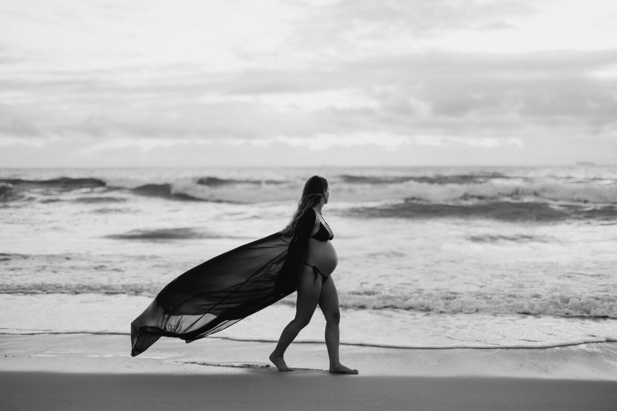 pregnant woman on the beach with a long veil floating behind her in the wind
