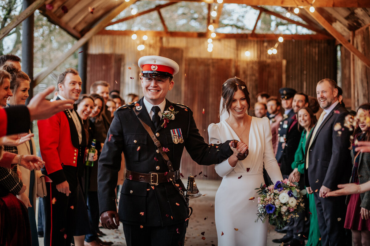 Bride and groom  wearing military uniform walk through a confetti tunnel at Silchester Farm
