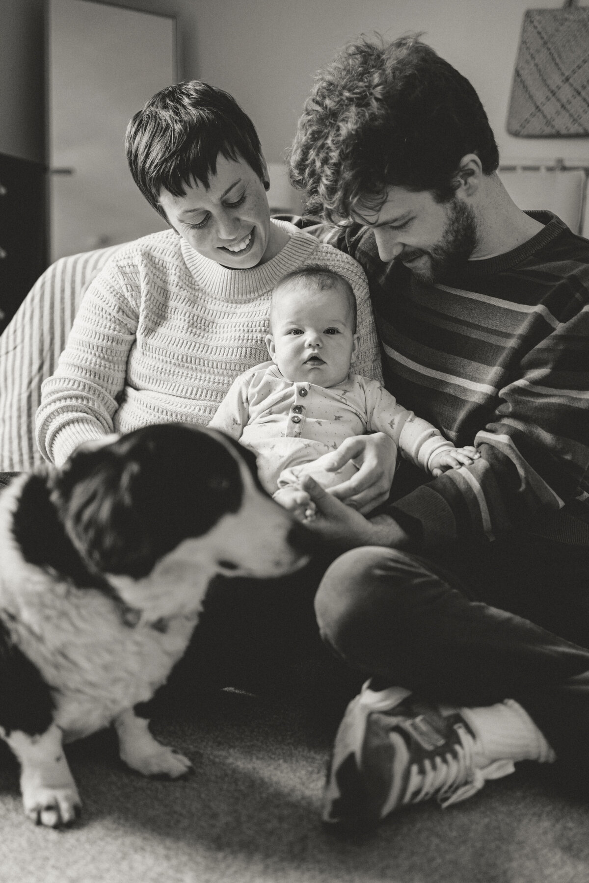 family of three and their dog looking at baby smiling during in home session with alexis adkins photo in longmont colorado