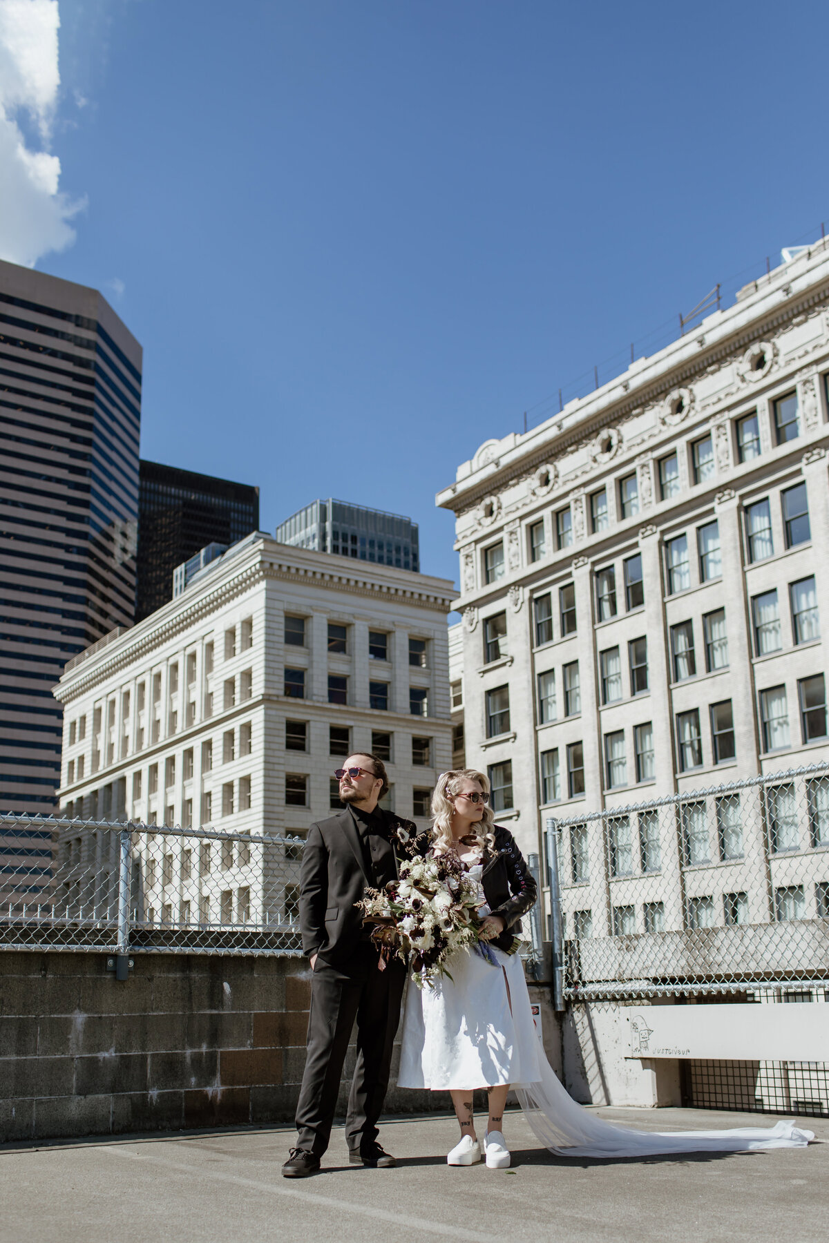 A cool bride and groom in sunglasses and a leather jacket on top of a Pioneer Square parking garage. Captured by Fort Worth Wedding Photographer, Megan Christine Studio