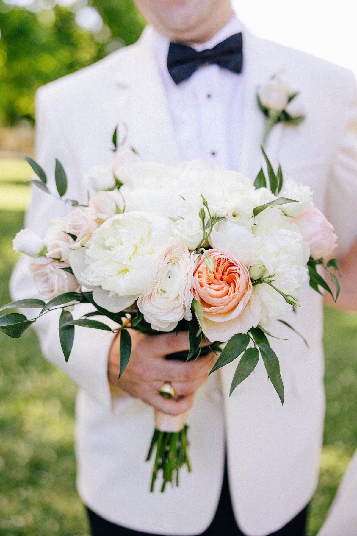 Groom in a white suit holding a bridal bouquet.