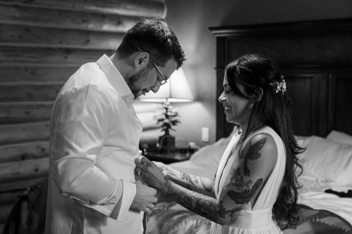 A bride helps her groom get ready in their hotel room in Wyoming.