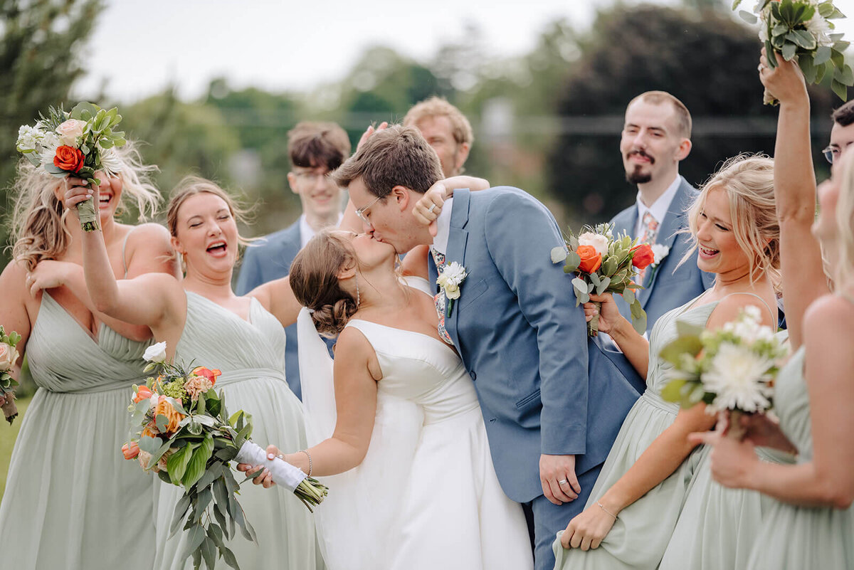 Bride and groom kissing whilst wedding party is cheering