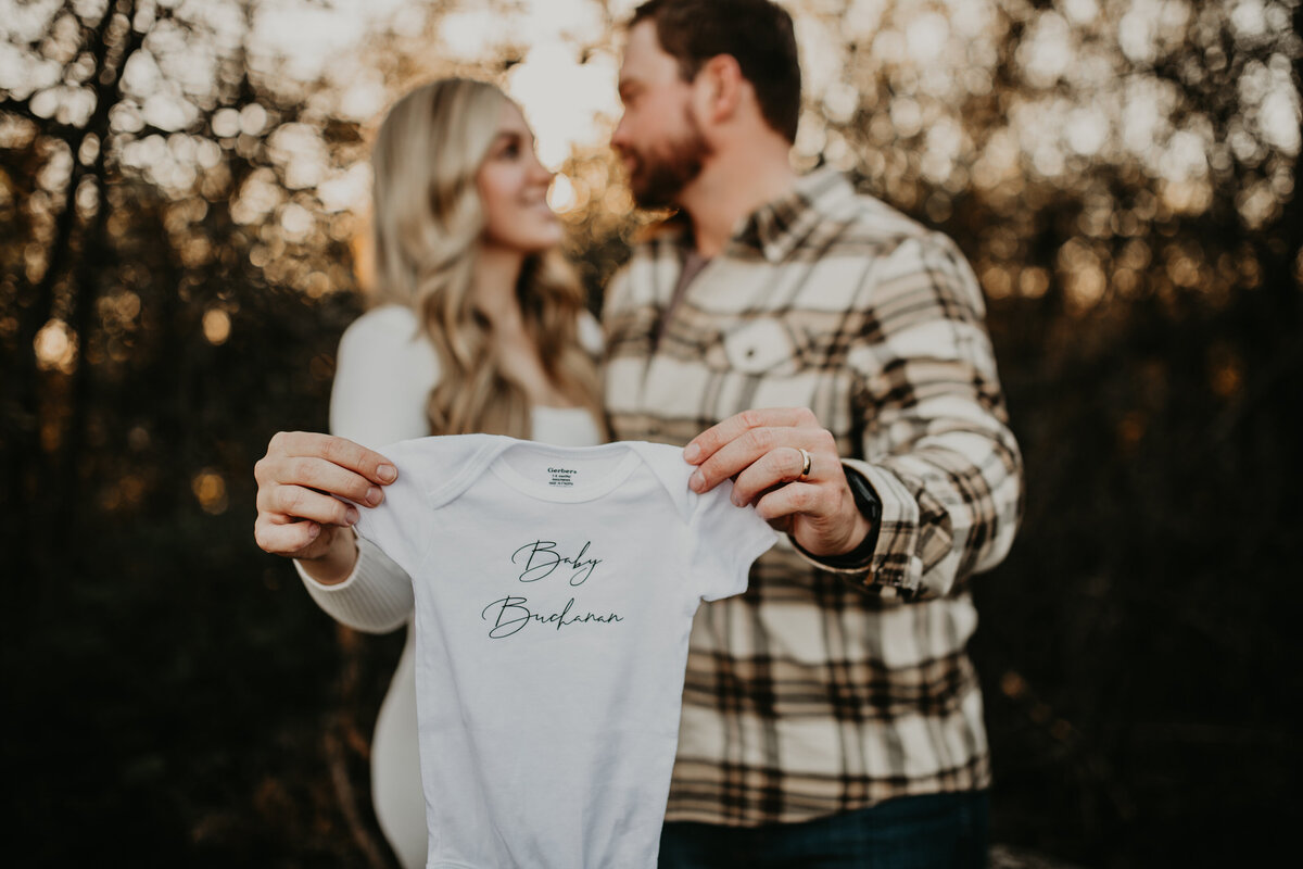 Expecting couple reveals pregnancy with onesie during a pregnancy announcement photography session in Fort Worth, Texas.