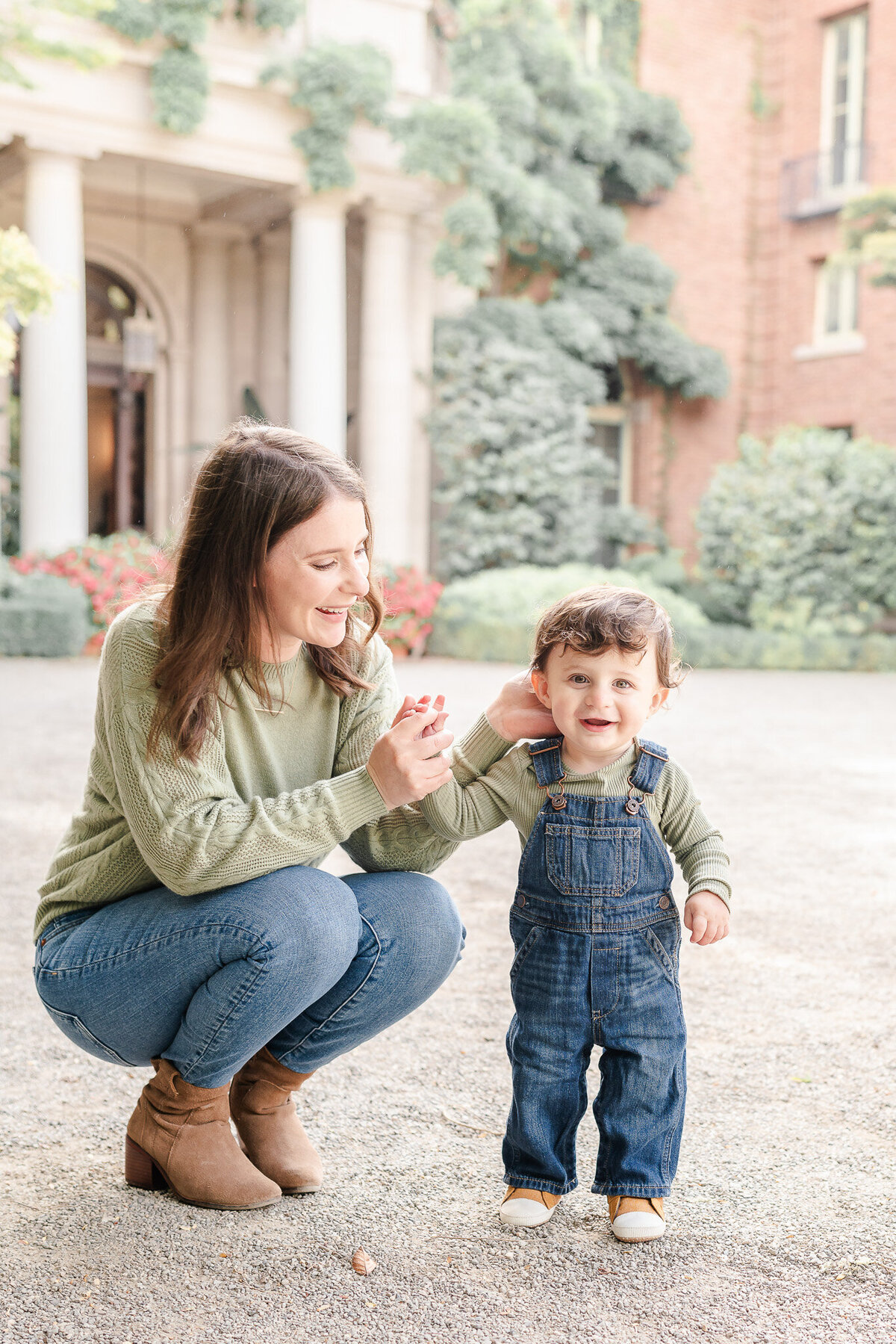 mom crouching down next to toddler son and smiling at him in front of filoli house