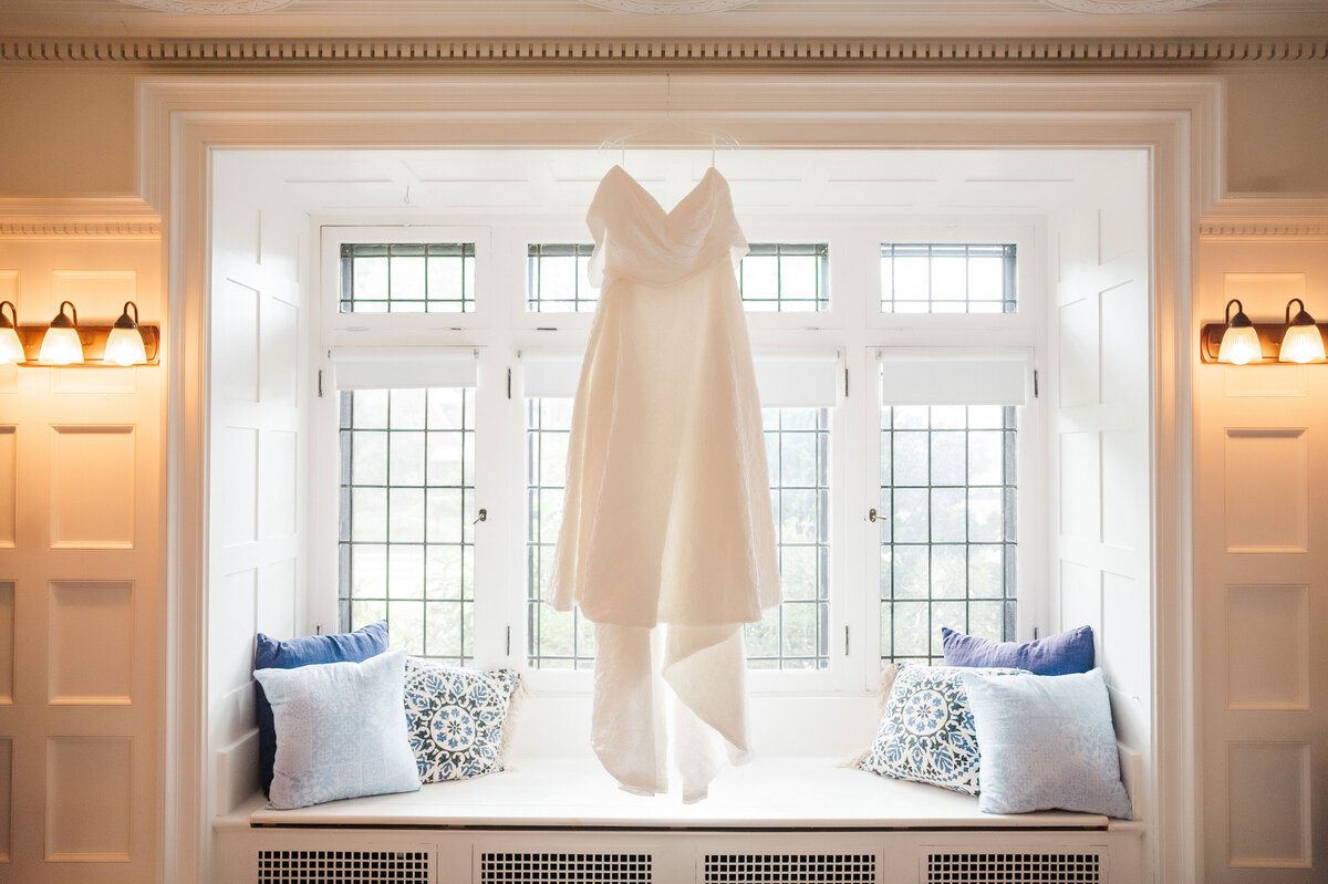 wedding dress hanging in the window before the wedding day at Frick Museum surrounded by lots of light and pillows