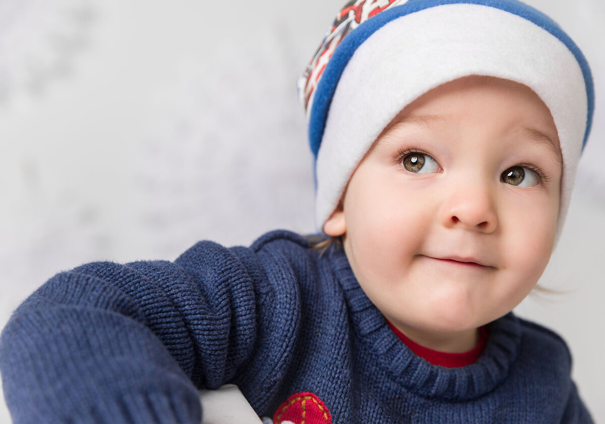 Image of a boy on a Christmas snowflake backdrop wearing a santa hat in the studio. Taken by Norwich portrait photographer Claire Howes. Christmas Mini Sessions Norwich.