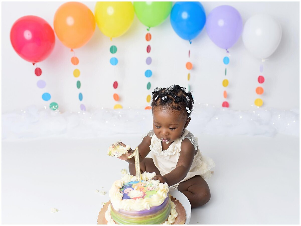 A little girl joyfully smashing a cake surrounded by colorful decorations.