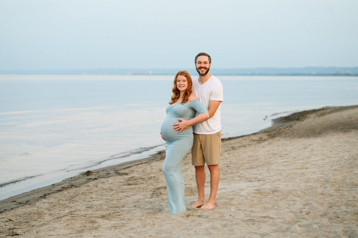 husband and wife cradling mom's belly on the beach for their summer maternity photos in Burlington, ON 