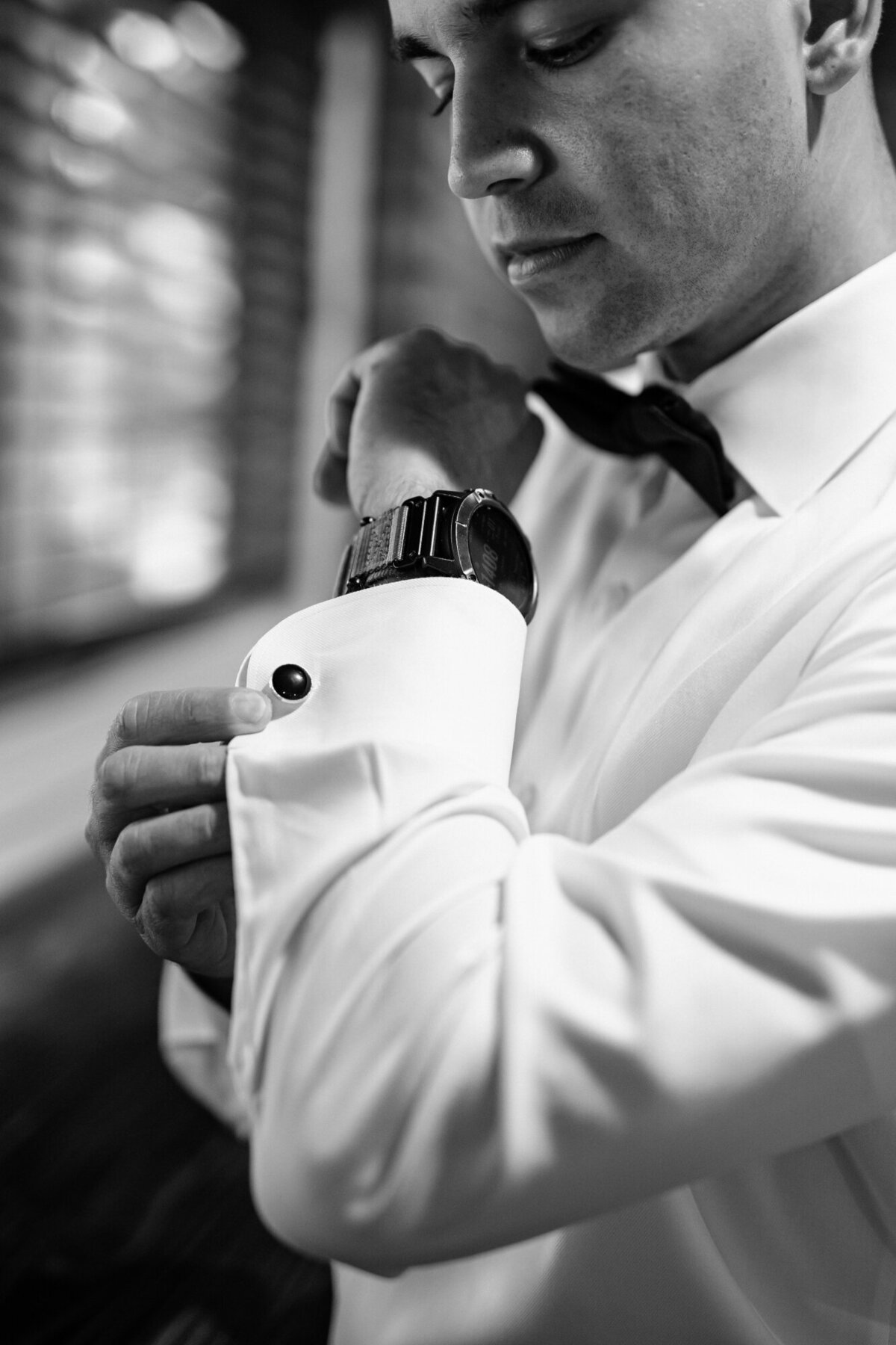 Black and white photo of the Groom putting his cufflinks on.