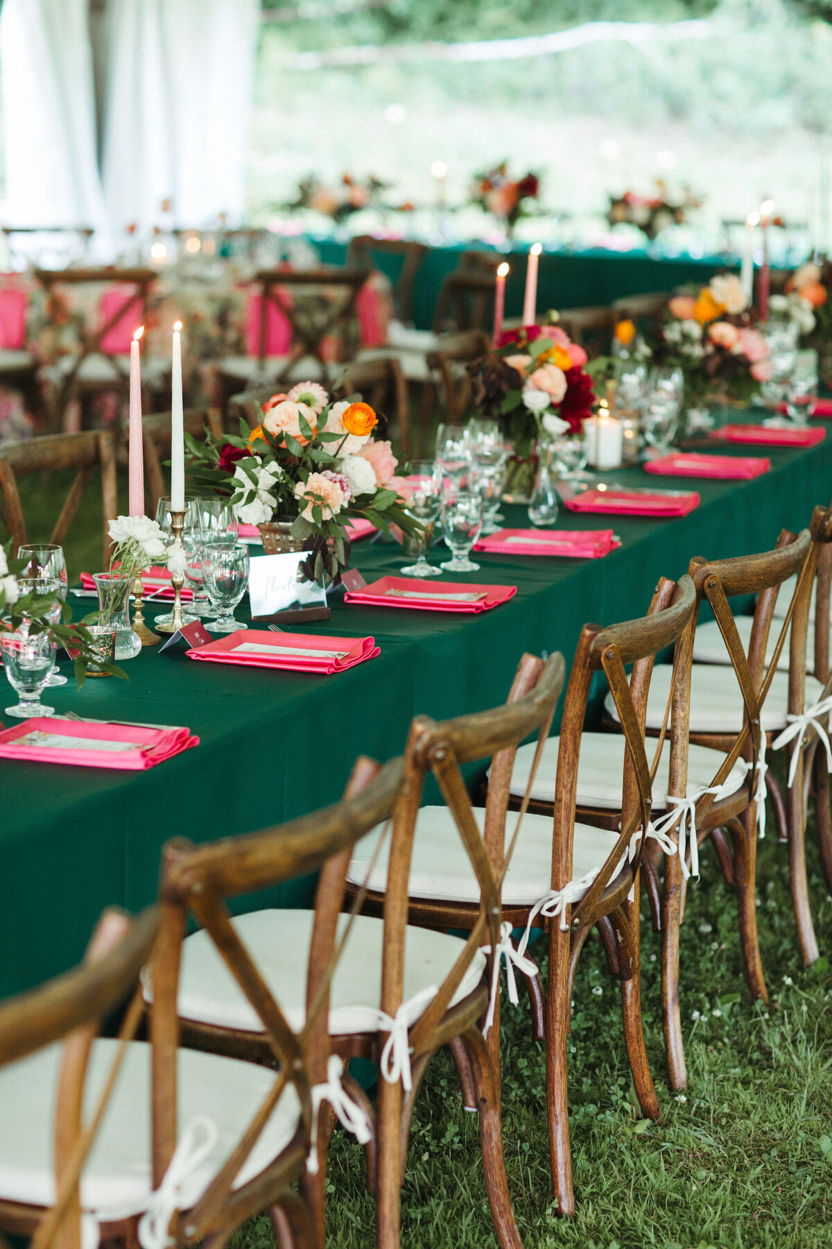 Harvest green guest tables with fuchsia napkins and vibrant florals in peach and burgundy are lined with wood crossback chairs under a tent for a wedding at Rockport Barn in Thousand Islands Ontario