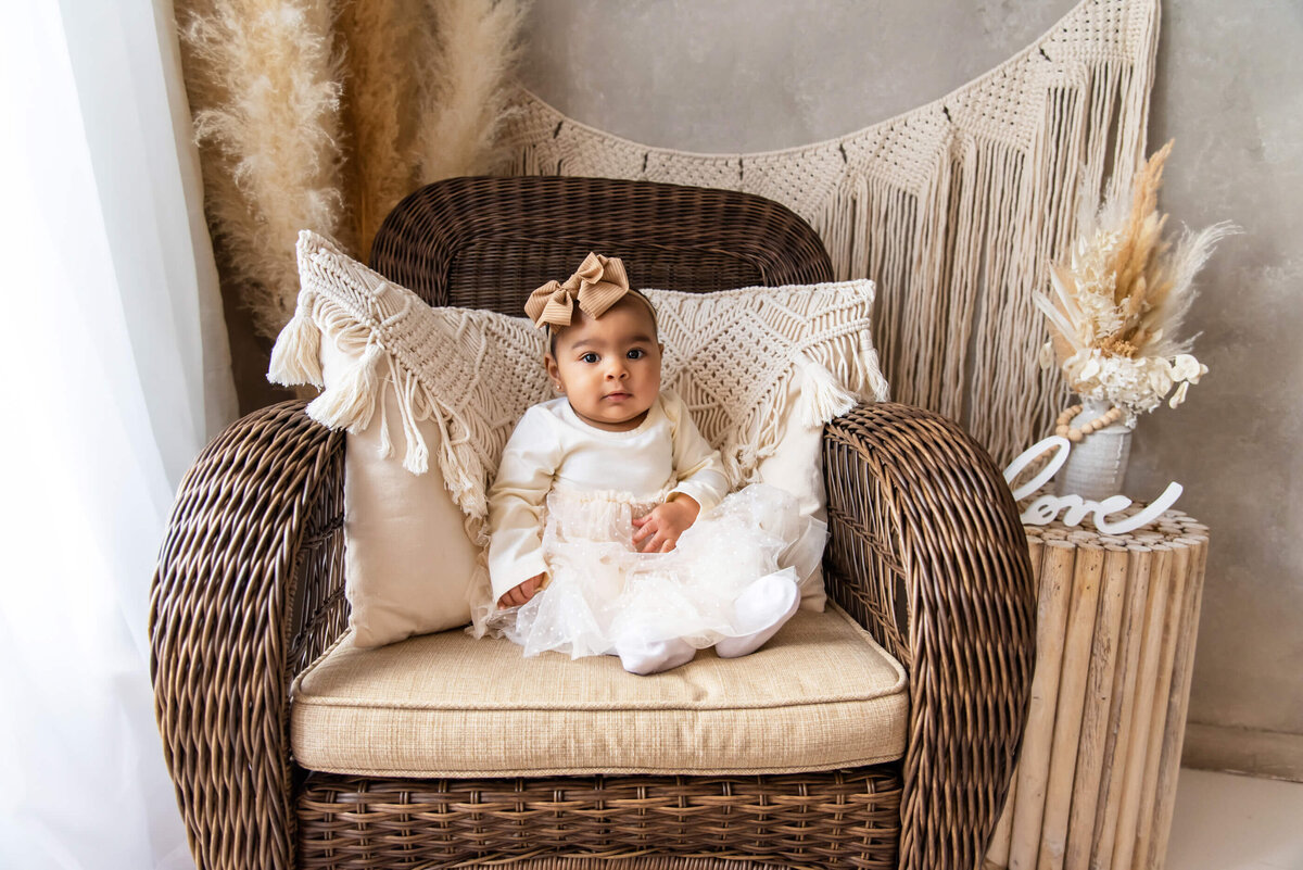 Black baby girl sitting in a rocking chair wearing a beige dress for her kids photography session in Burlington, ON