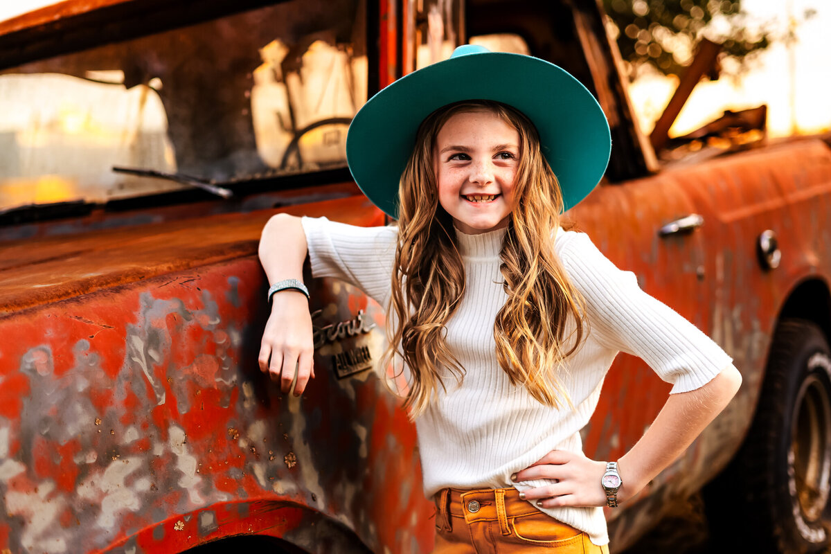 Young girl leaning on an old orange truck in fall season