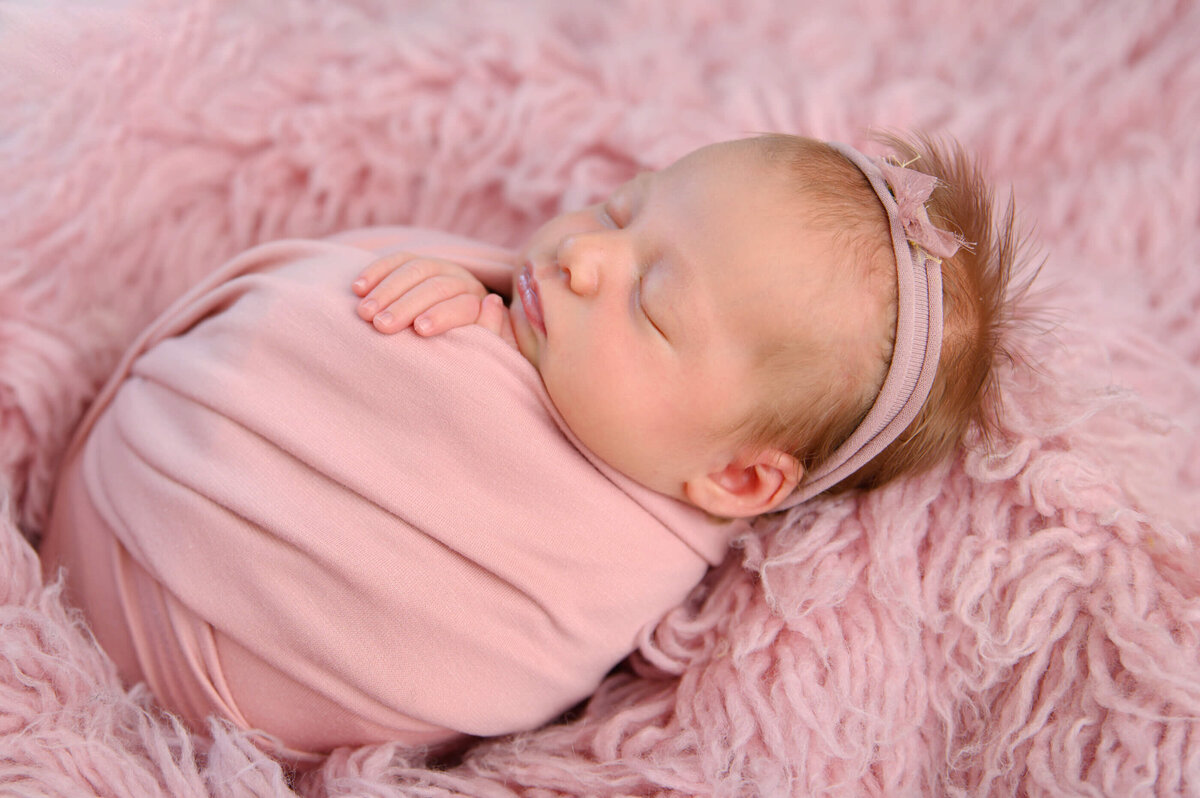 side angle photo of a newborn girl wrapped in pink on a pink rug for her newborn photos in Burlington, Ontario