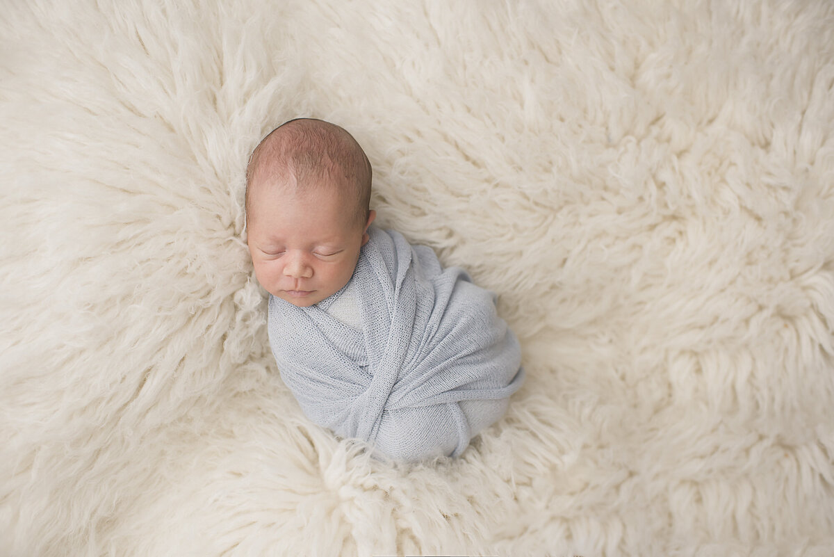 a tightly wrapped newborn laying on white fur