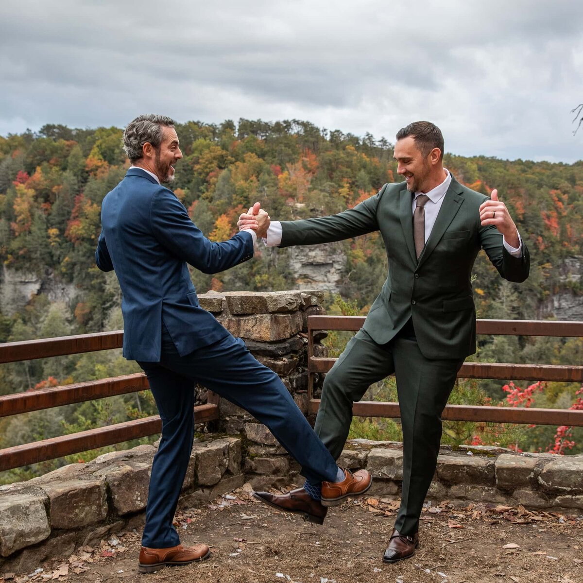 Two men in suits dance together at a mountainous overlook at State Park during the wedding celebration.